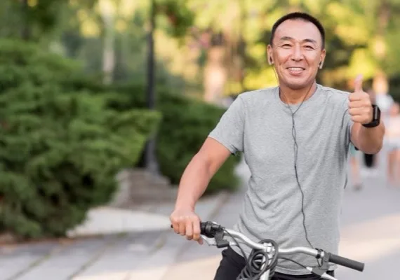 Homem de meia-idade sorrindo sobre uma bicicleta, num parque